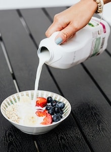 Someone pouring milk on a bowl of berries