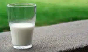 Glass of milk on a sidewalk with a grassy area behind it