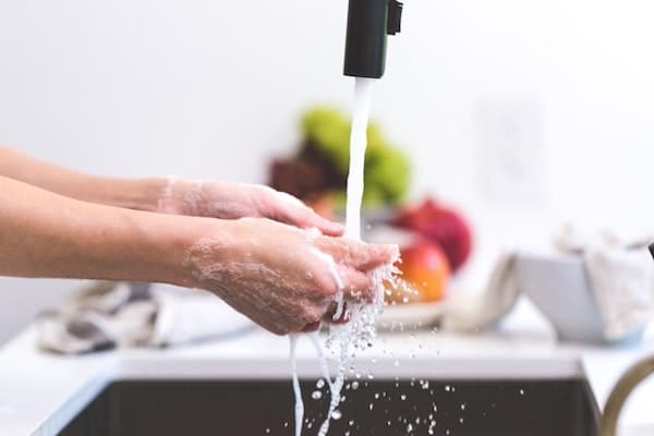person washing hands at a kitchen sink with food in the background