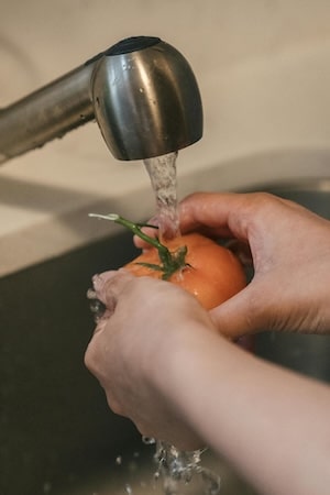 Person washing tomato in the kitchen sink